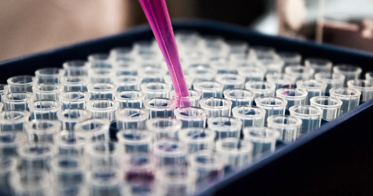 Magenta reagent dripping into rows of glass vials in a chemistry lab