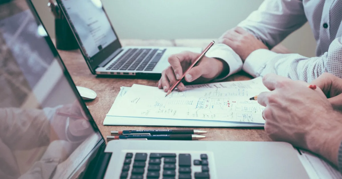 Two people reviewing market-entry plans on paper and laptop