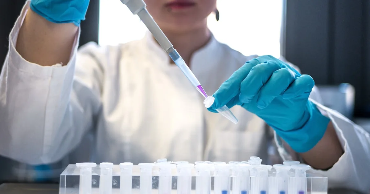 Lab technician in blue gloves pipetting a sample for quality control